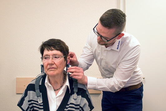 Ein Hörakustiker passt einer älteren Frau ein Hörgerät zur Hörtest-Diagnose an.